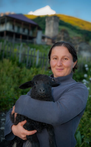 Adishi, Svaneti / Georgia - July 23, 2017: Local woman holding a black lamb in her village with Mt Tetnuldi in background.
