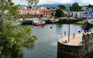 Children jumping from breakwater in harbor of Puerto de Alba, Asturias, Spain