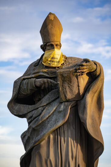 Statue of Saint Bruno on the Alte Mainbrücke (Old Main Bridge) of Würzburg, Germany with a facemask with words 'Avoid Corona'