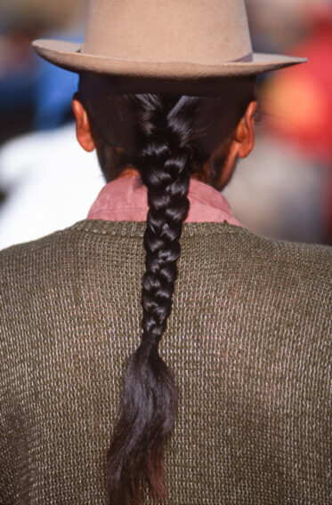 An indigenous man with long braided black hair from the Volcan Chimborazo area near Riobamba, Ecuador at the weekly outdoor animal market.