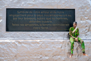 Standing at 30 metres, the Amazon Monument in Cotonou is an incredible tribute to the female warriors of Dahomey. With a rifle in hand and a defiant gaze, the Amazon embodies the strength, courage, and resilience of these legendary women.
Unveiled in 2022, the statue was commissioned by the Beninese government as part of an effort to reclaim and honor its pre-colonial history. It stands near the Place de l’Amazone, a key site in Cotonou’s ongoing cultural renaissance. It is meant as a statement: Benin’s past is not forgotten, and its female warriors remain a source of national pride.