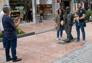Oviedo, Asturias, Spain - August 10, 2020: Tourists posing with bronze statue of Woody Allen designed by Spanish sculptor Vincente Menendez Santarua on a pedestrian walkway.