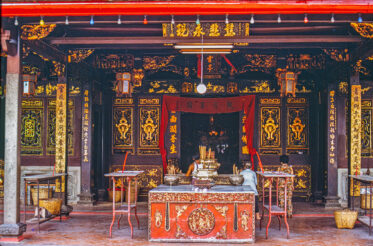 Inside Cheng Hoon Teng Temple, Malacca — ornate gilded carvings, red lanterns, and worshippers tending the incense-filled altar of one of Malaysia's oldest functioning Chinese temples.